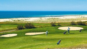 Ein Golfplatz mit Sandbunkern, Blick auf das Meer und eine Person beim Golfen.