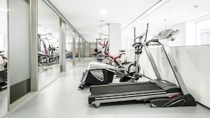 Une salle de sport moderne équipée de divers appareils d’exercice, notamment des tapis de course et des vélos d’appartement, et dotée d’un mur en verre sur l’un des côtés.