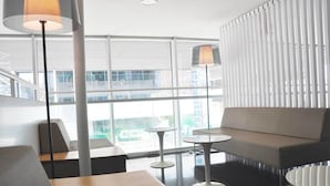 Un espace lounge moderne, doté de sièges, de tables et de grandes fenêtres offrant une vue sur la ville.