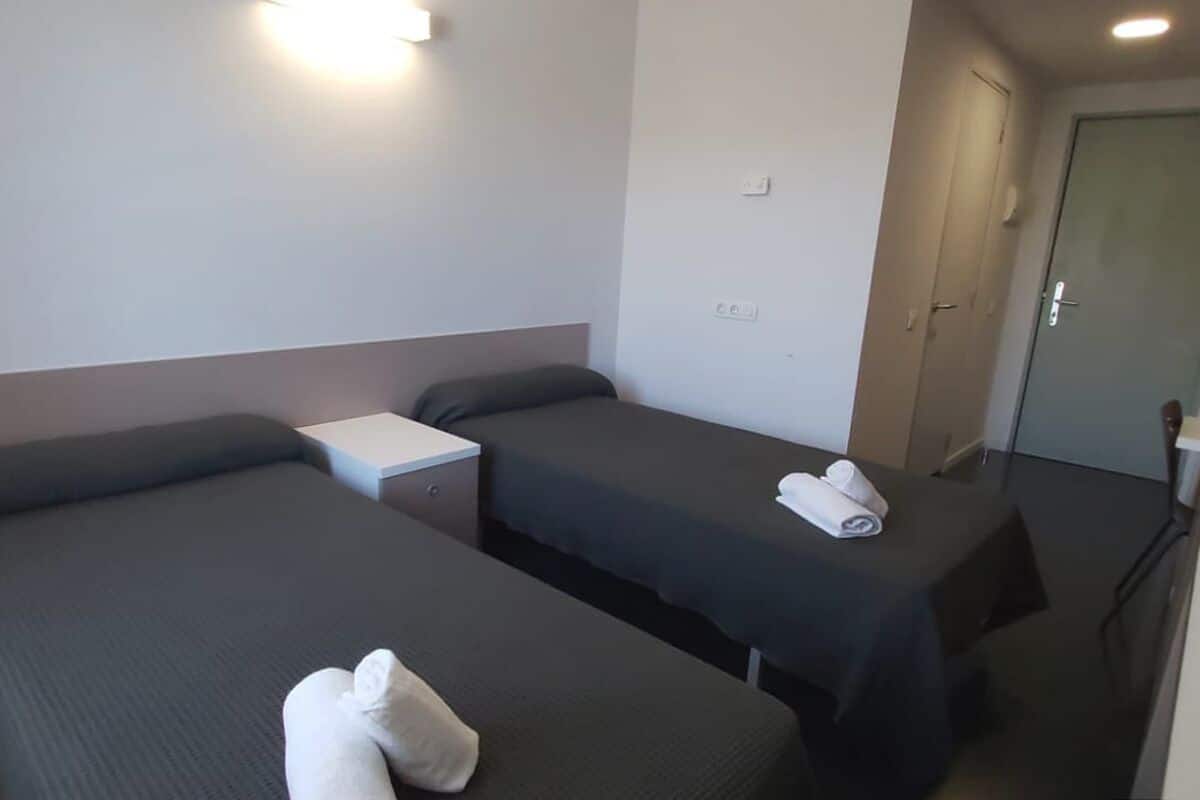 Een hotelkamer met twee enkele bedden, een klein nachtkastje en een deur aan de rechterkant.