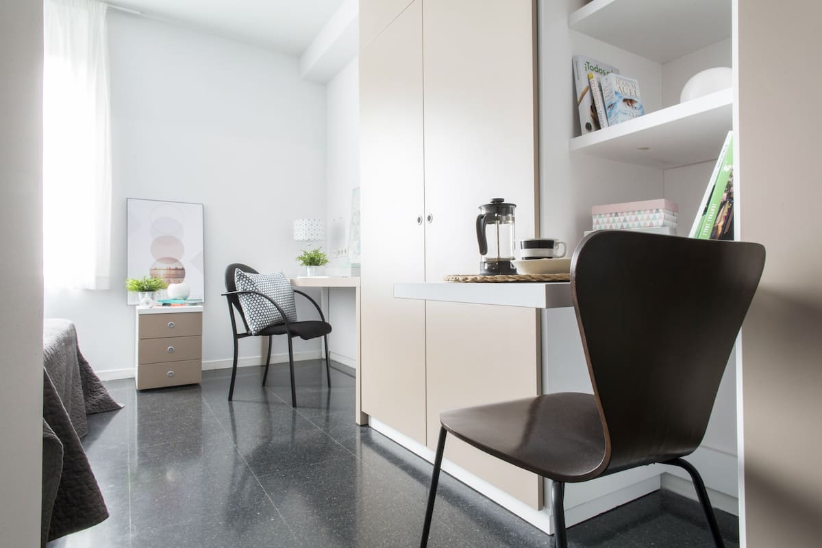 Een moderne, goed verlichte kamer met een bureau, twee stoelen, een boekenkast en een raam met gordijnen.