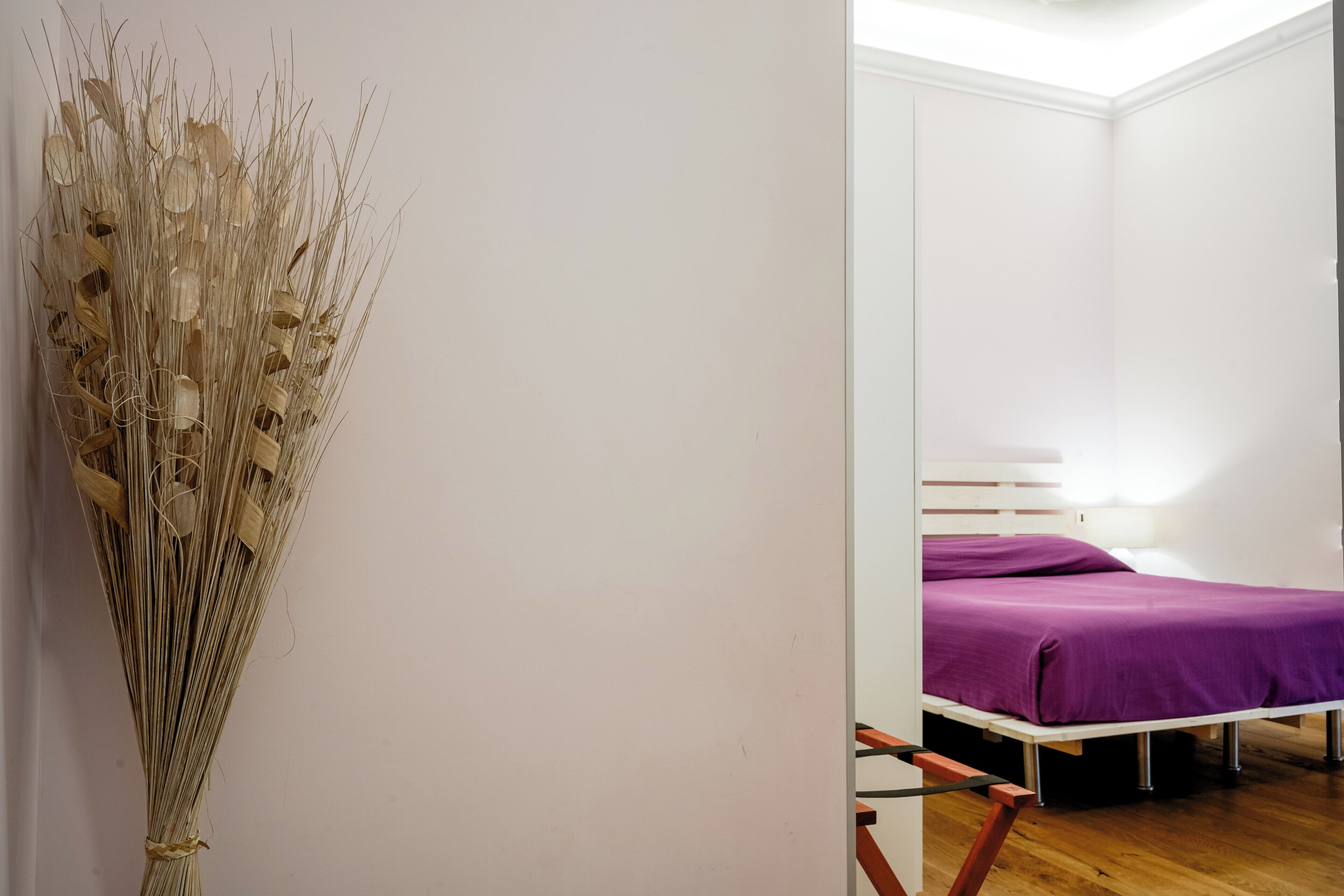 Una habitación con una cama, una silla y un arreglo decorativo de plantas secas.
