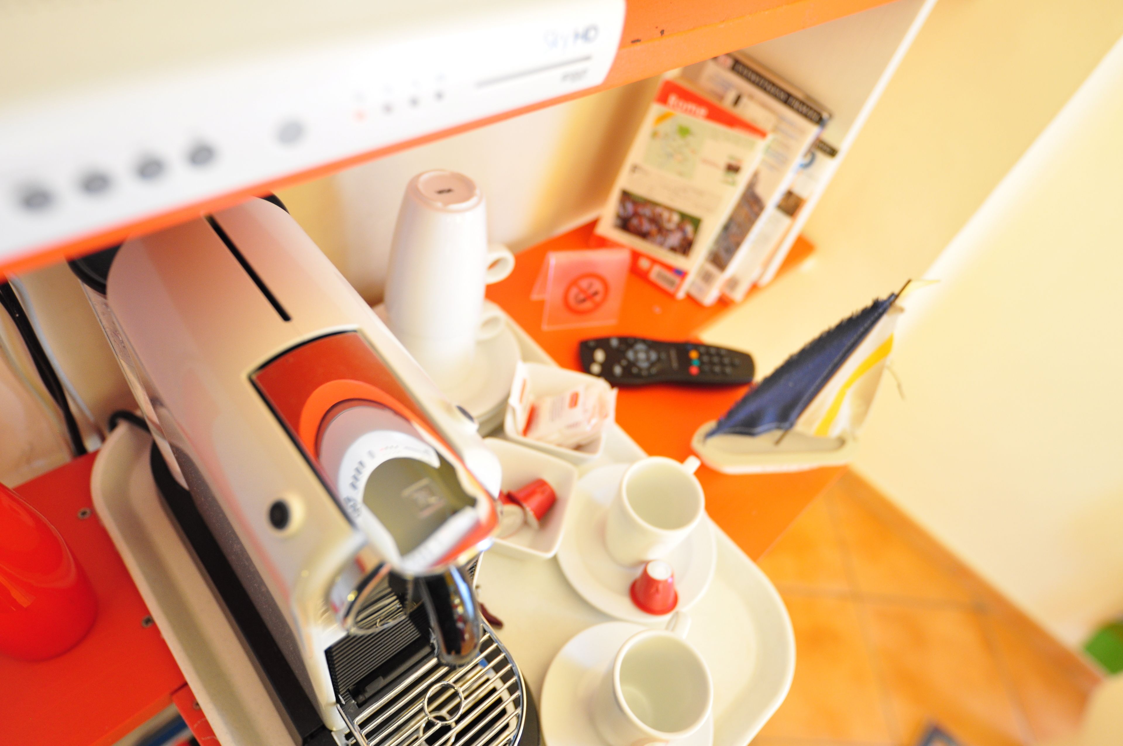 A coffee machine, cups, and a remote control on a table.