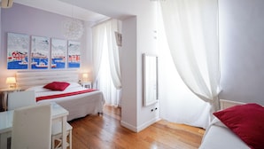 Habitación de hotel con cama, escritorio y silla. Hay cuadros en la pared y una ventana con cortinas.