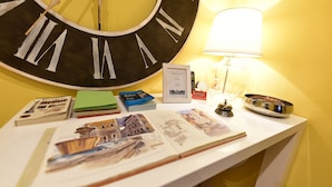 Una mesa con un gran reloj de pared, libros, postales y un diploma enmarcado.