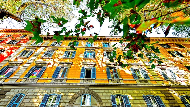 Un edificio de varios pisos con fachada amarilla y contraventanas azules, que presenta un ventanal central arqueado y varios balcones.