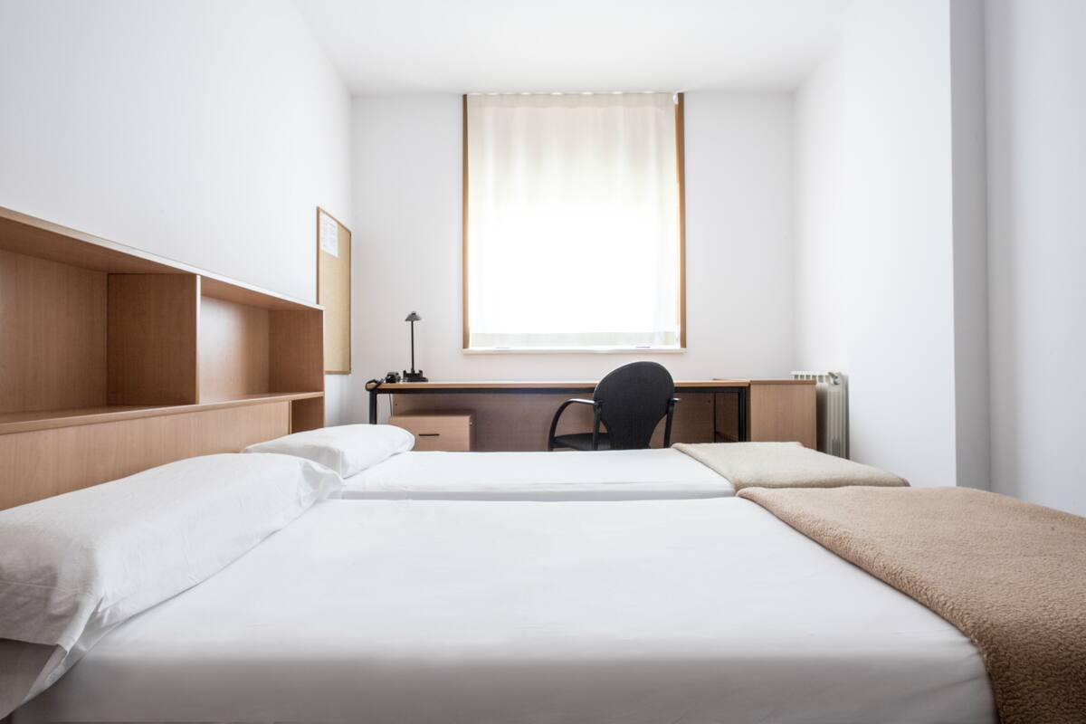 Une chambre d’hôtel avec un lit, un bureau, une chaise et une fenêtre avec des rideaux.