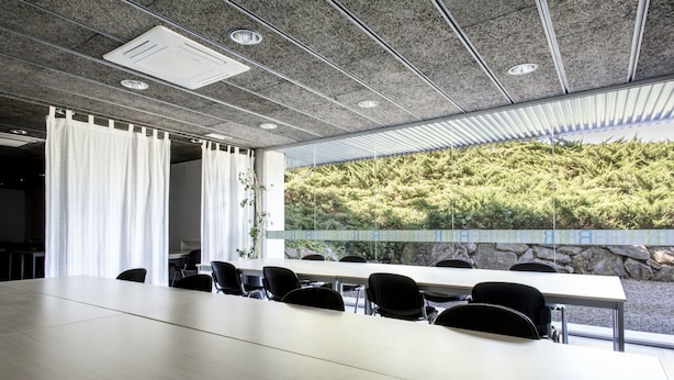 A conference room with a long table and chairs, a large window with a view of a forested hillside, and a ceiling with recessed lighting and air vents. - Residencia Universitaria Resa Campus de Montilivi (Girona)