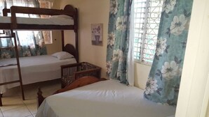 A dormitory room with bunk beds, a crib, and a window with floral curtains.