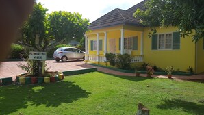 A yellow house with a car parked in front, surrounded by greenery and a sign that reads "ALMOND TREE VILLA".