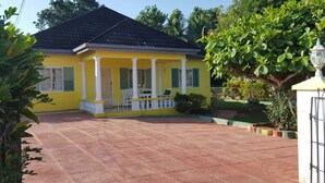 A yellow house with a tiled driveway and a covered porch with white columns.