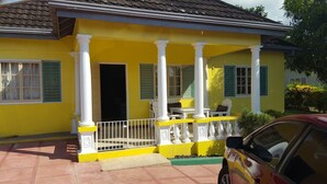 A yellow house with a porch, white columns, and a car parked in front.