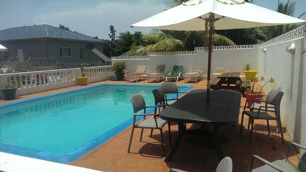 A backyard with a swimming pool, a table with chairs, and a covered area with an umbrella.
