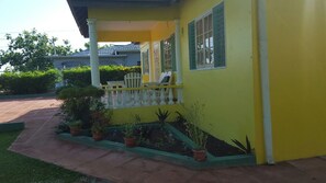 A yellow house with a porch, potted plants, and a pathway leading to the entrance.