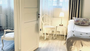 A room with a bed, a desk with a lamp, a chair, and a door.