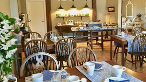 A dining area with wooden tables and chairs, a kitchen in the background, and hanging pendant lights. - Hotel Hamngatan 27 (Falkenberg)