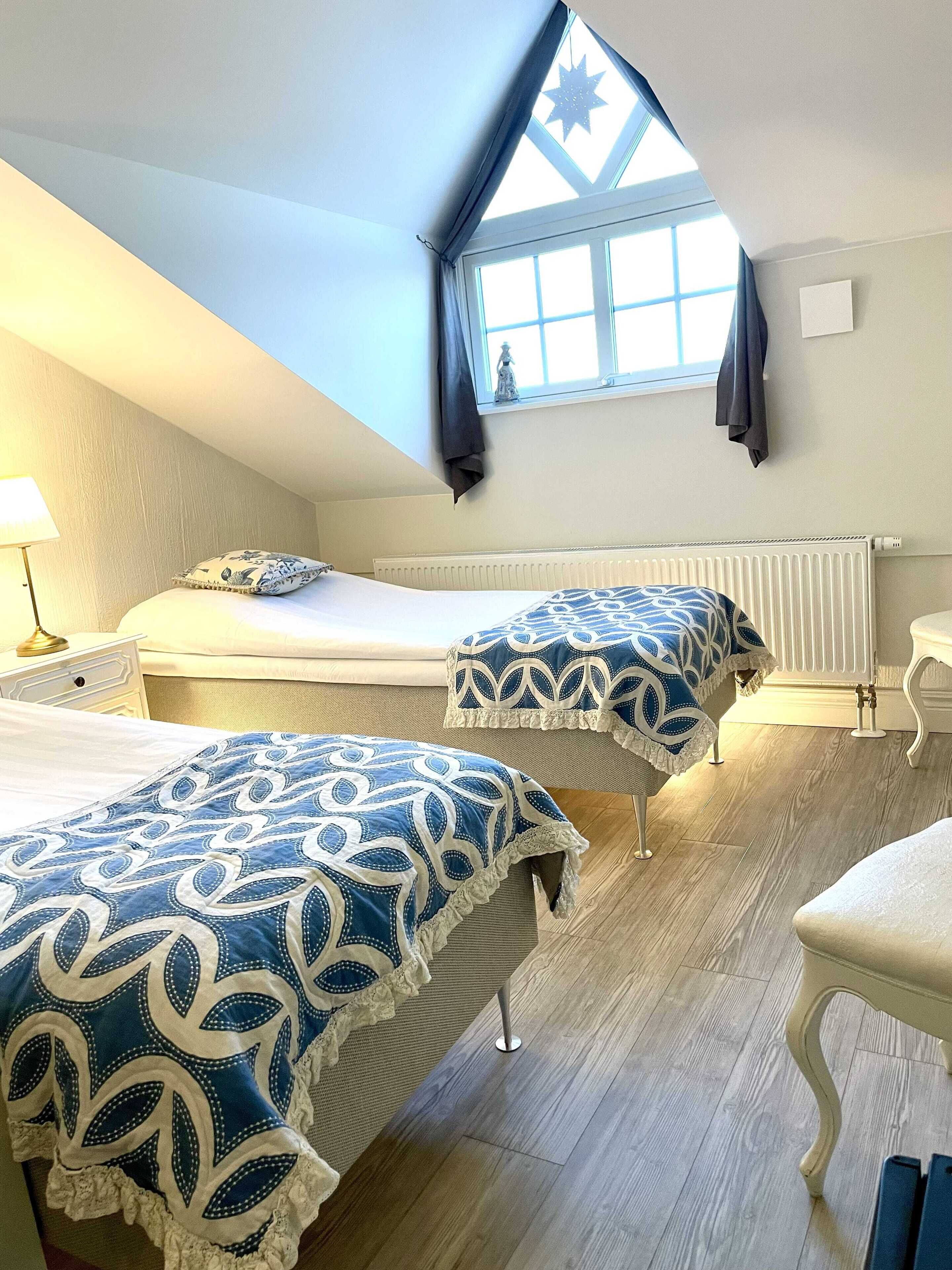 A bedroom with two beds, a window with a star decoration, a radiator, and a lamp.