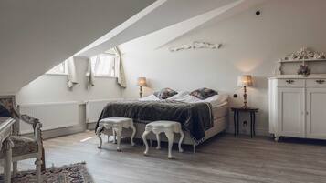 A bedroom with a sloped ceiling, a bed with a dark quilt, two bedside tables with lamps, a white wardrobe, and a patterned rug.