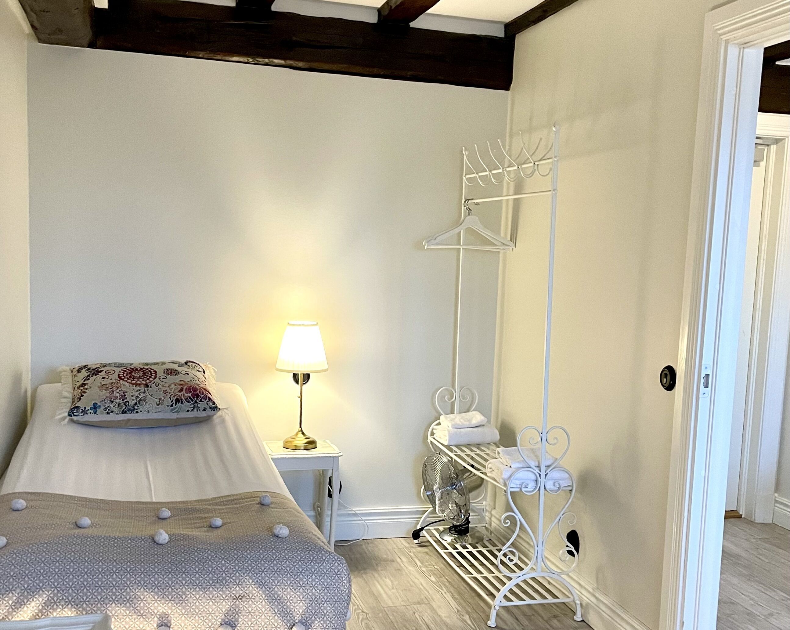 Quarto com cama, luminária de cabeceira, cabideiro e pequena mesa com abajur.