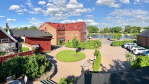 A large brick building with a red roof, surrounded by a well-maintained lawn and a parking area with several cars. - Hotel Hamngatan 27 (Falkenberg)