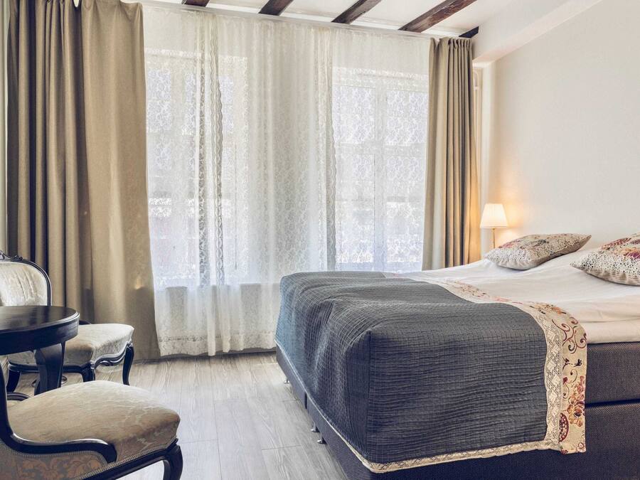 A hotel room with a bed, a chair, a table, and a lamp.