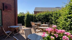 An outdoor patio with wooden tables and chairs, surrounded by gravel and greenery. - Hotel Hamngatan 27 (Falkenberg)