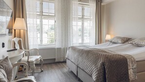 A bedroom with a large bed, two chairs, a table, and a window with curtains. - Hotel Hamngatan 27 (Falkenberg)