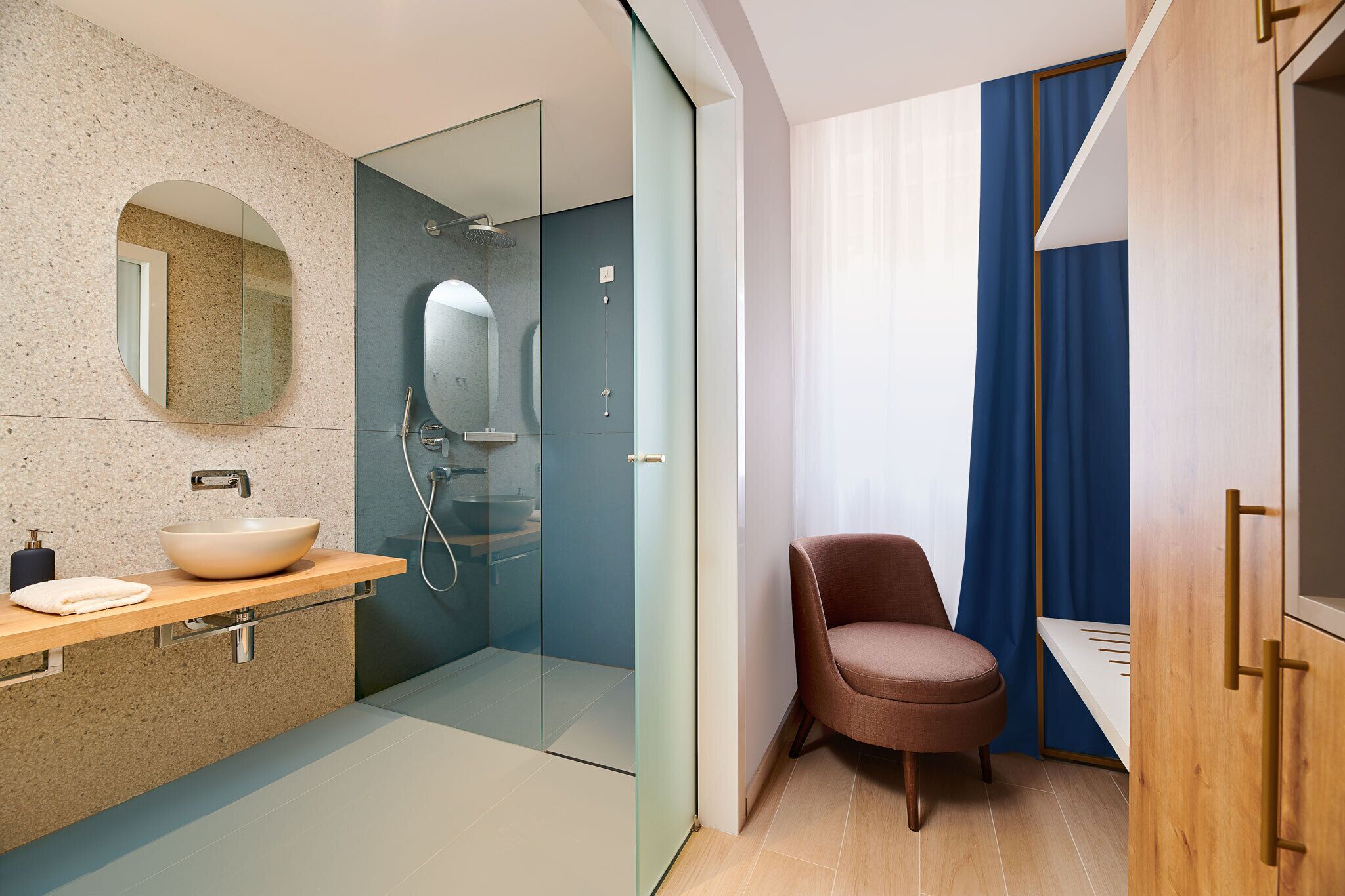 A modern bathroom with a glass shower enclosure, a round mirror, and a wooden vanity.