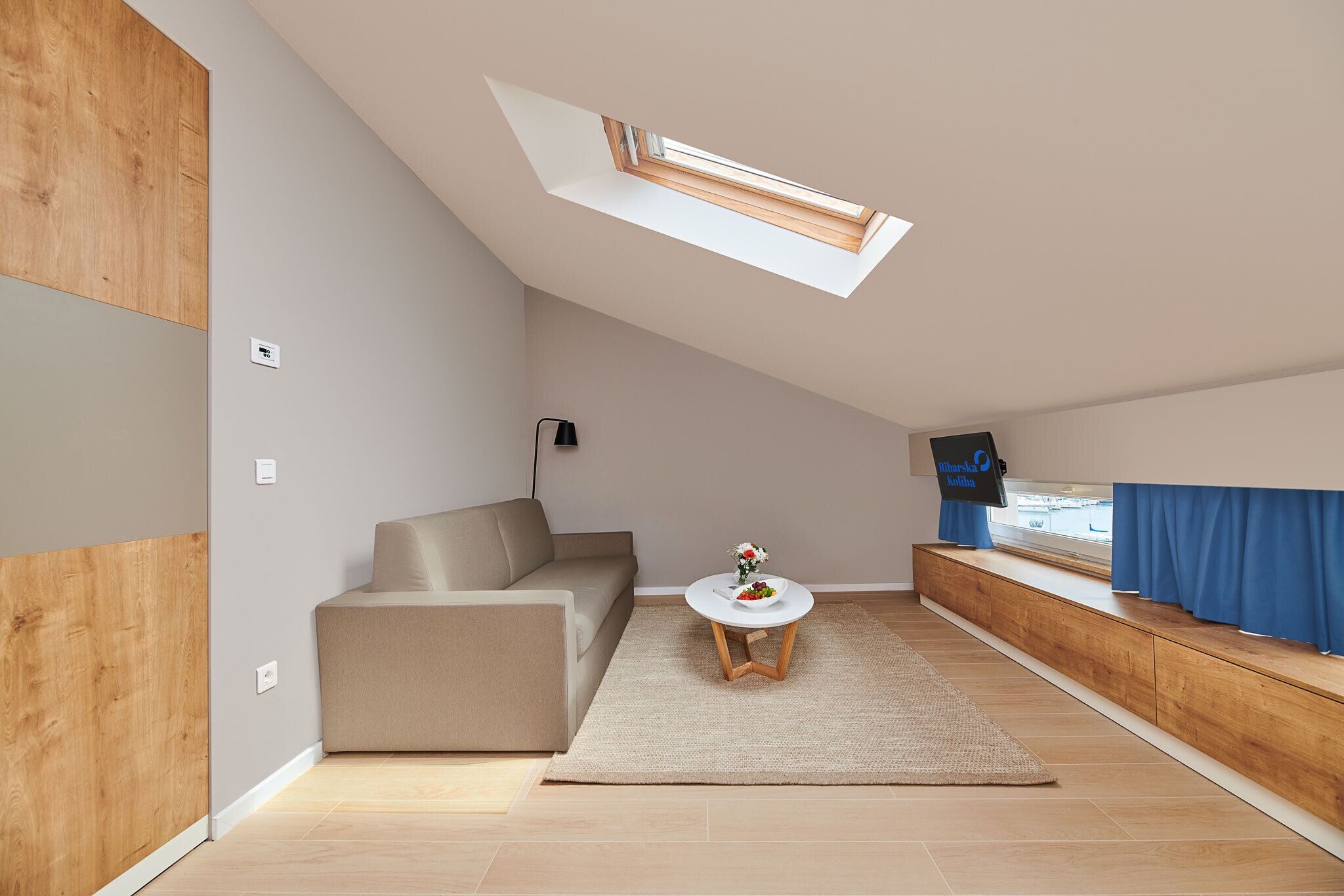 Et moderne loftværelse med skrå vægge, en indbygget bænk ved vinduet, en sofa og et lille bord med en vase.