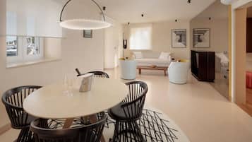 Una sala moderna con una mesa de comedor redonda, sillas negras, un sofá blanco y un amplio ventanal con vista a barcos.