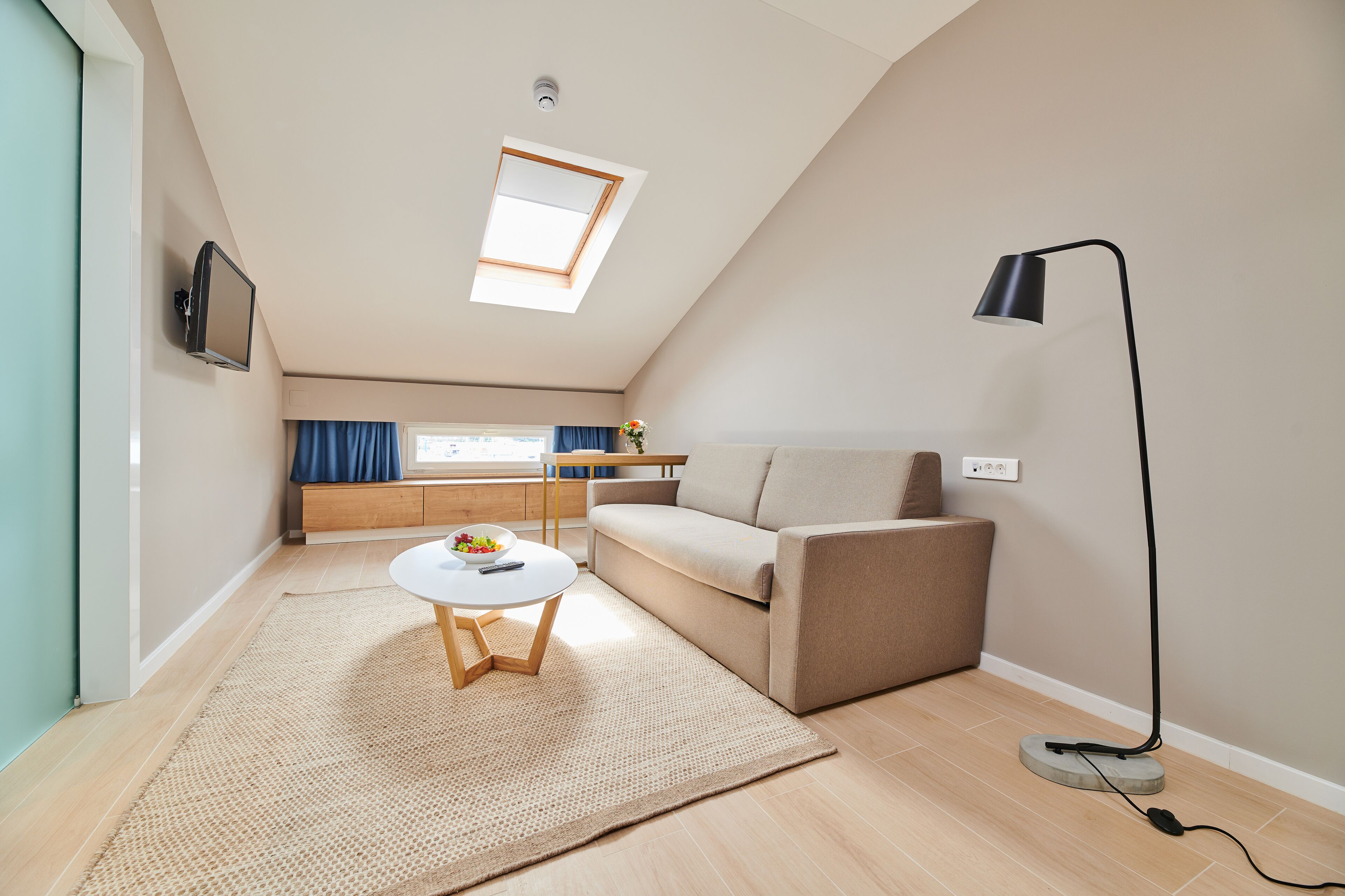 A modern living room with a sofa, a coffee table, a lamp, and a TV mounted on the wall.