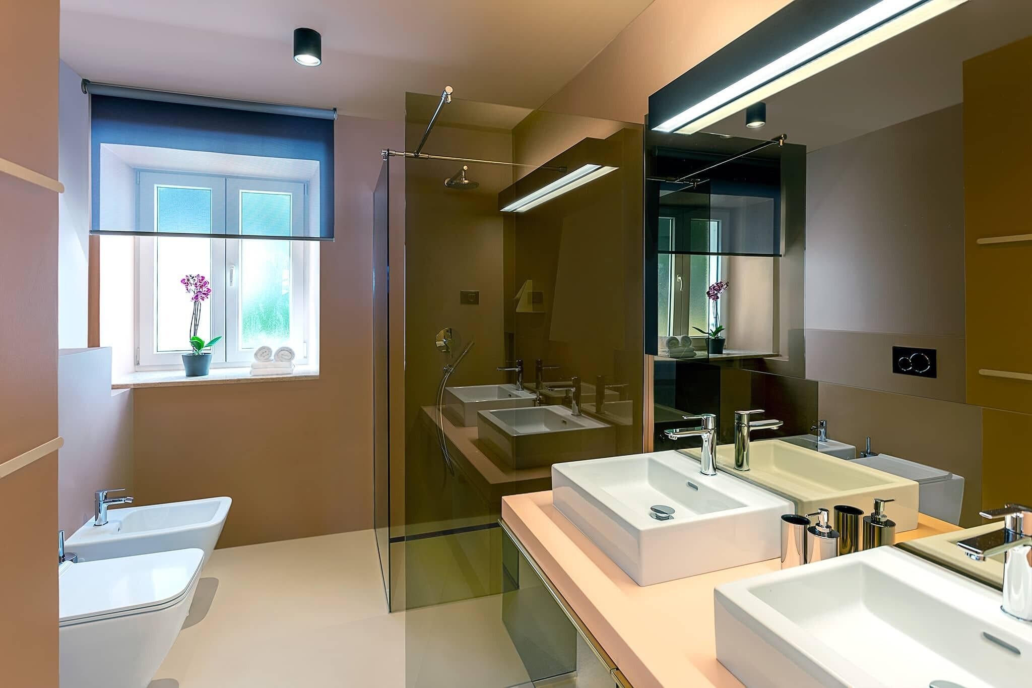 Ein modernes Badezimmer mit einer Duschkabine, zwei Waschbecken und einem großen Spiegel.