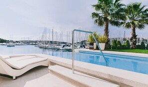A pool area with lounge chairs, a palm tree, and a marina in the background.