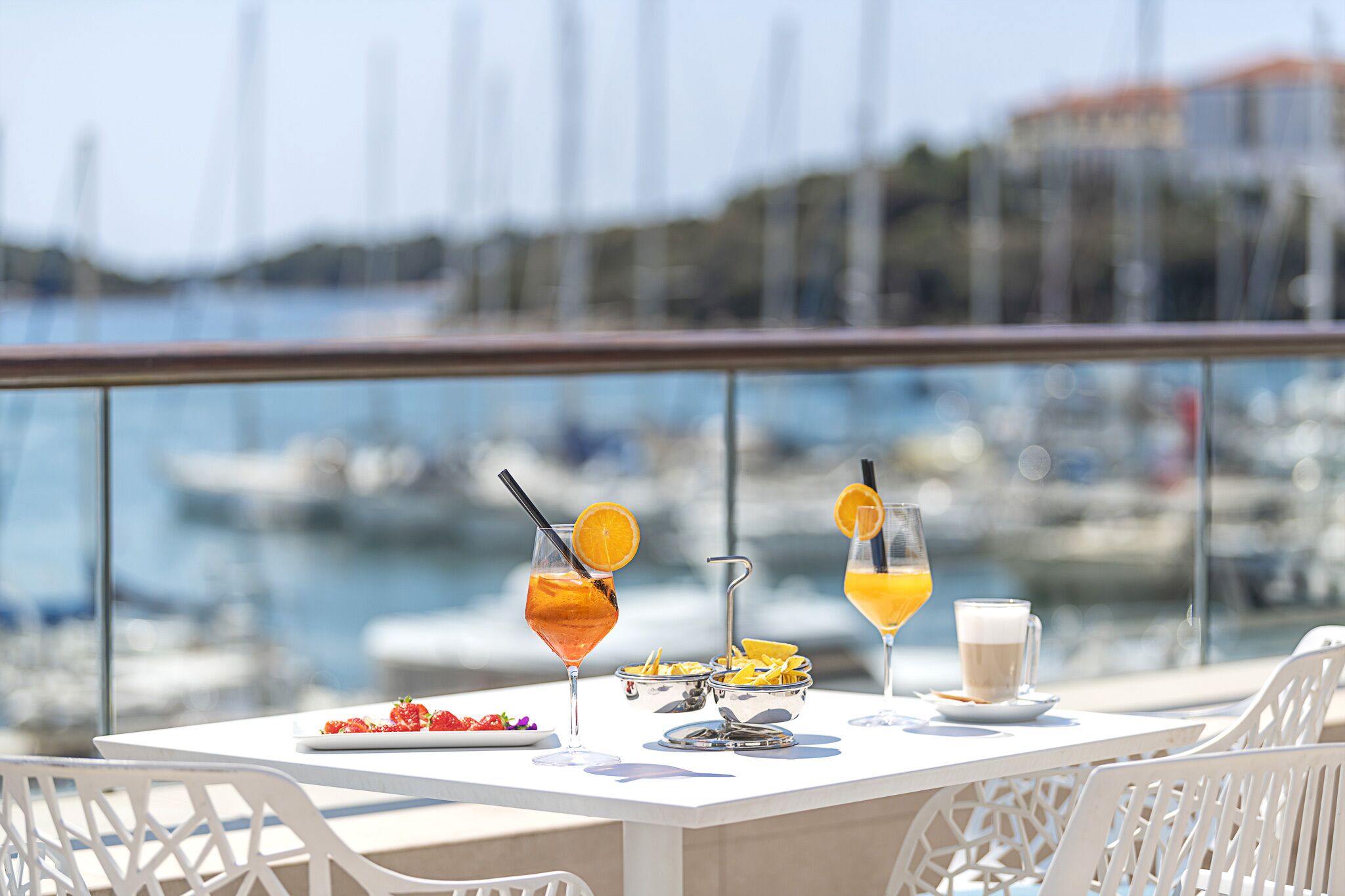 A table with drinks and snacks, overlooking a marina with boats.