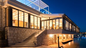 A modern building with large glass windows, a stone facade, and a waterfront view. - Ribarska Koliba Resort (Pula)