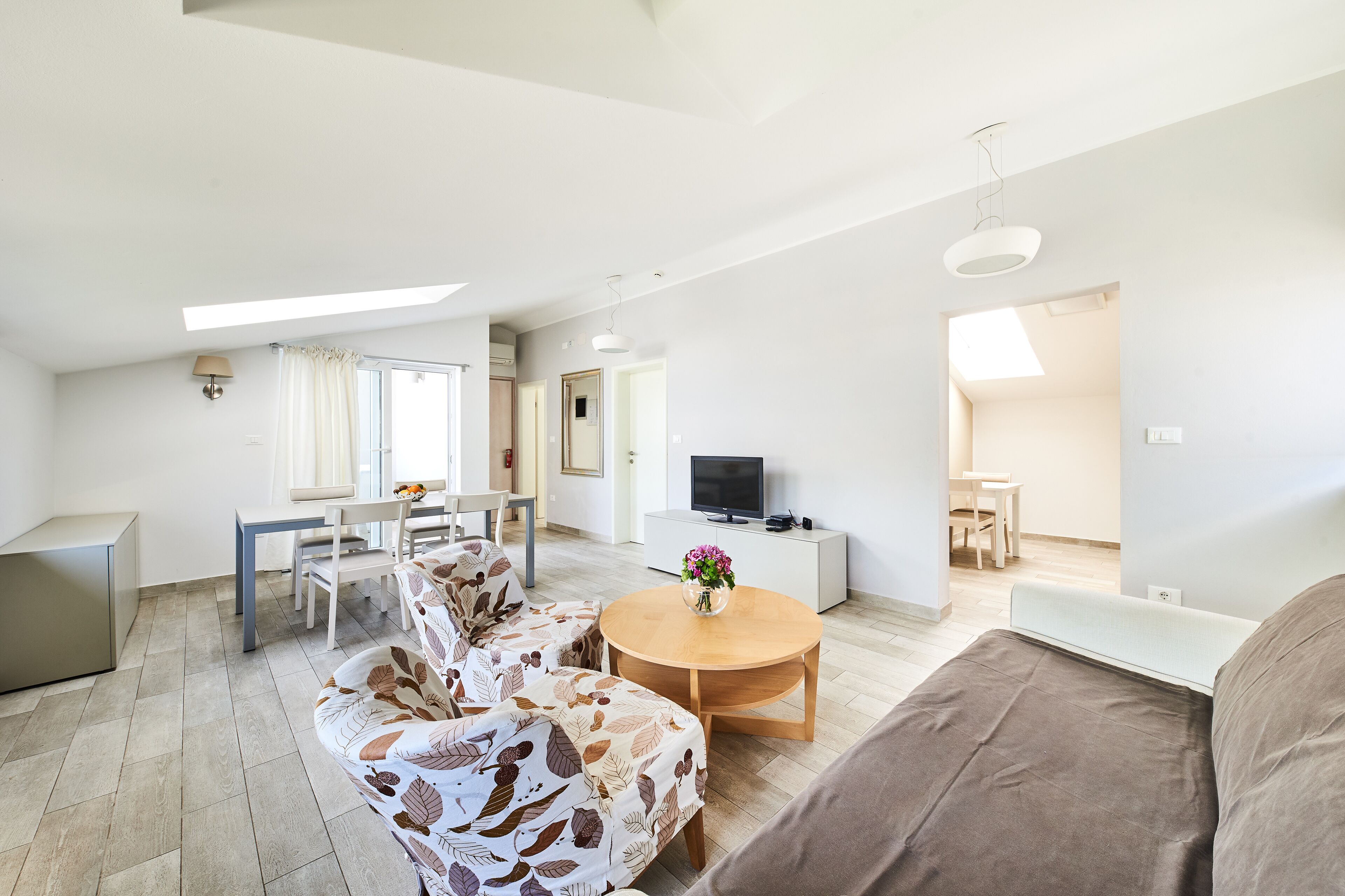 Una sala de estar moderna con un sofá, una mesa redonda de madera y un televisor sobre un mueble blanco.