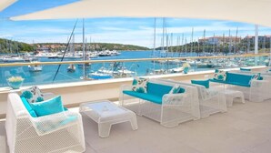 A terrace with white wicker furniture and teal cushions, overlooking a marina with boats and buildings in the background. - Ribarska Koliba Resort (Pula)