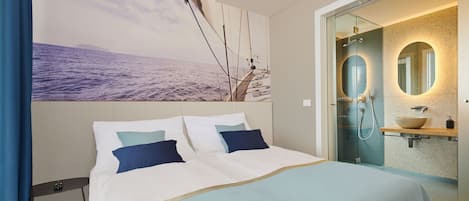 Habitación de hotel moderna con una cama grande, un baño con paredes de vidrio y un mural panorámico en la pared.