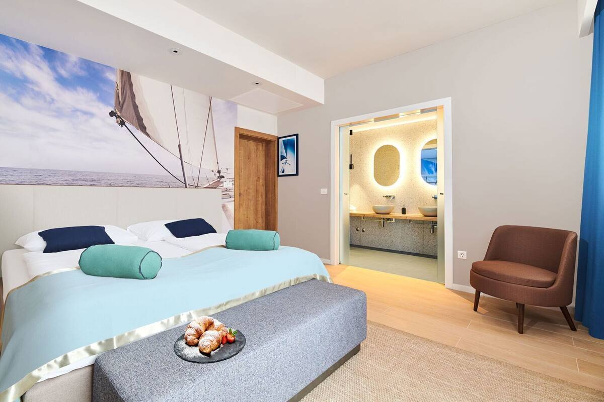A modern bedroom with a bed, a chair, a breakfast tray, and a view of a bathroom.