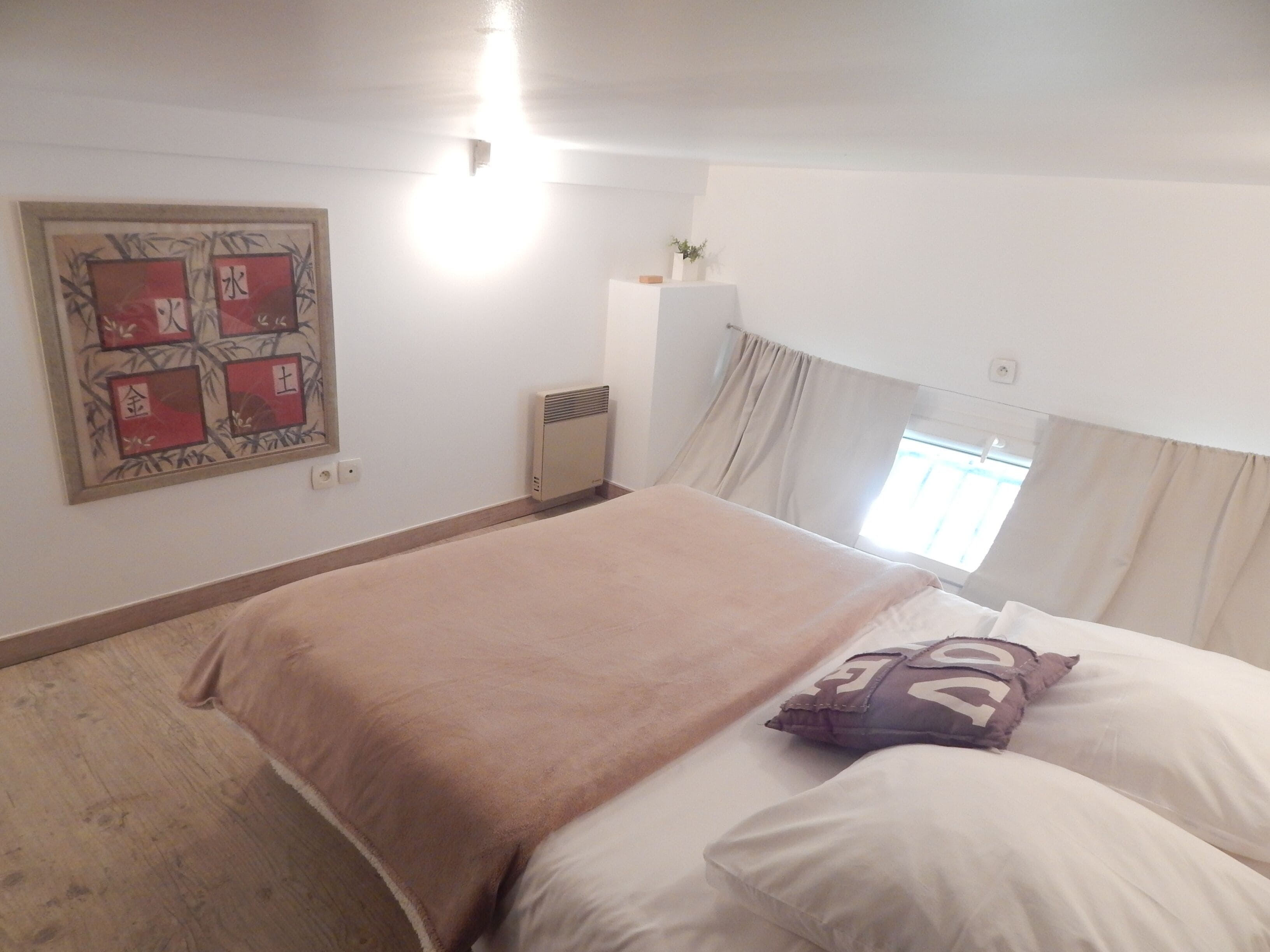 A bedroom with a large bed, a radiator, a window with curtains, and a wall-mounted artwork.