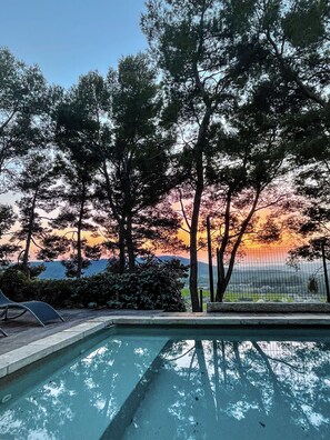 A swimming pool with a view of trees and a sunset.