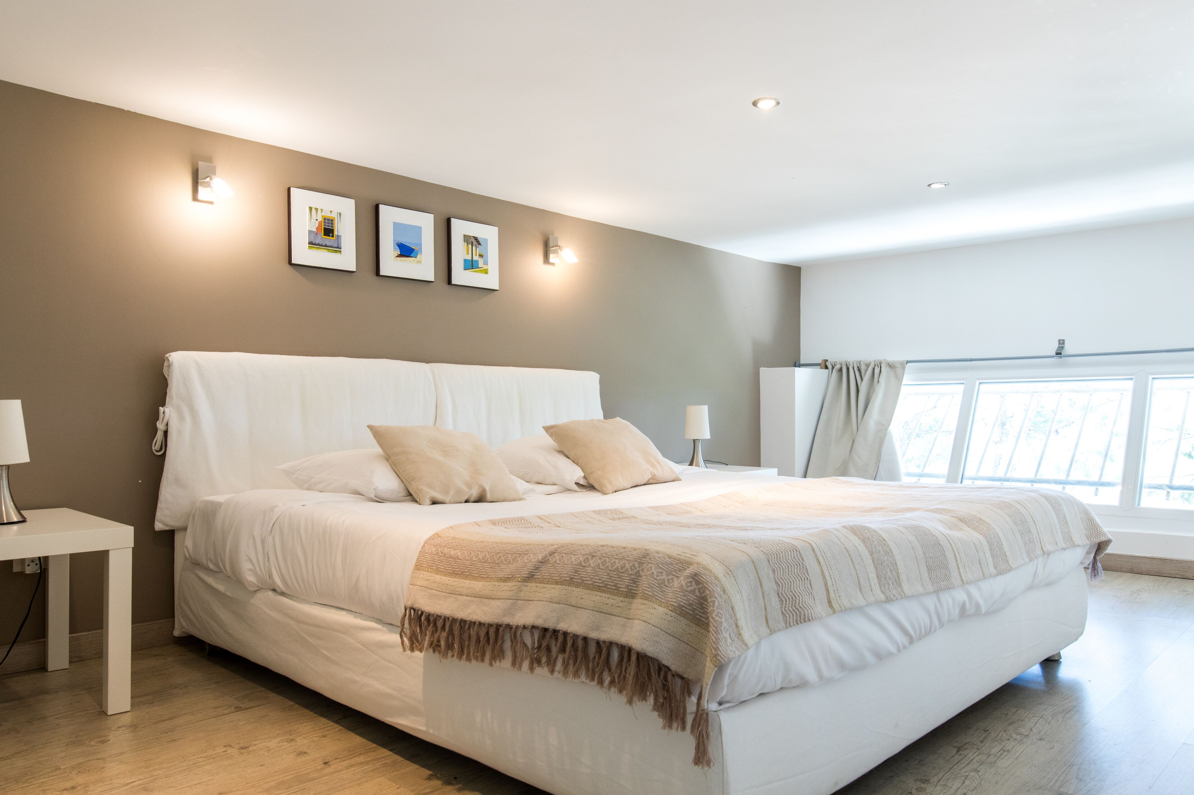 A modern bedroom with a large bed, bedside tables, and wall-mounted lights.