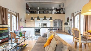 A spacious living area with a sofa, chairs, a coffee table, and a dining table. There is a kitchen in the background with modern appliances and a dining area with chairs. - Le Mas des Roches (Velaux)
