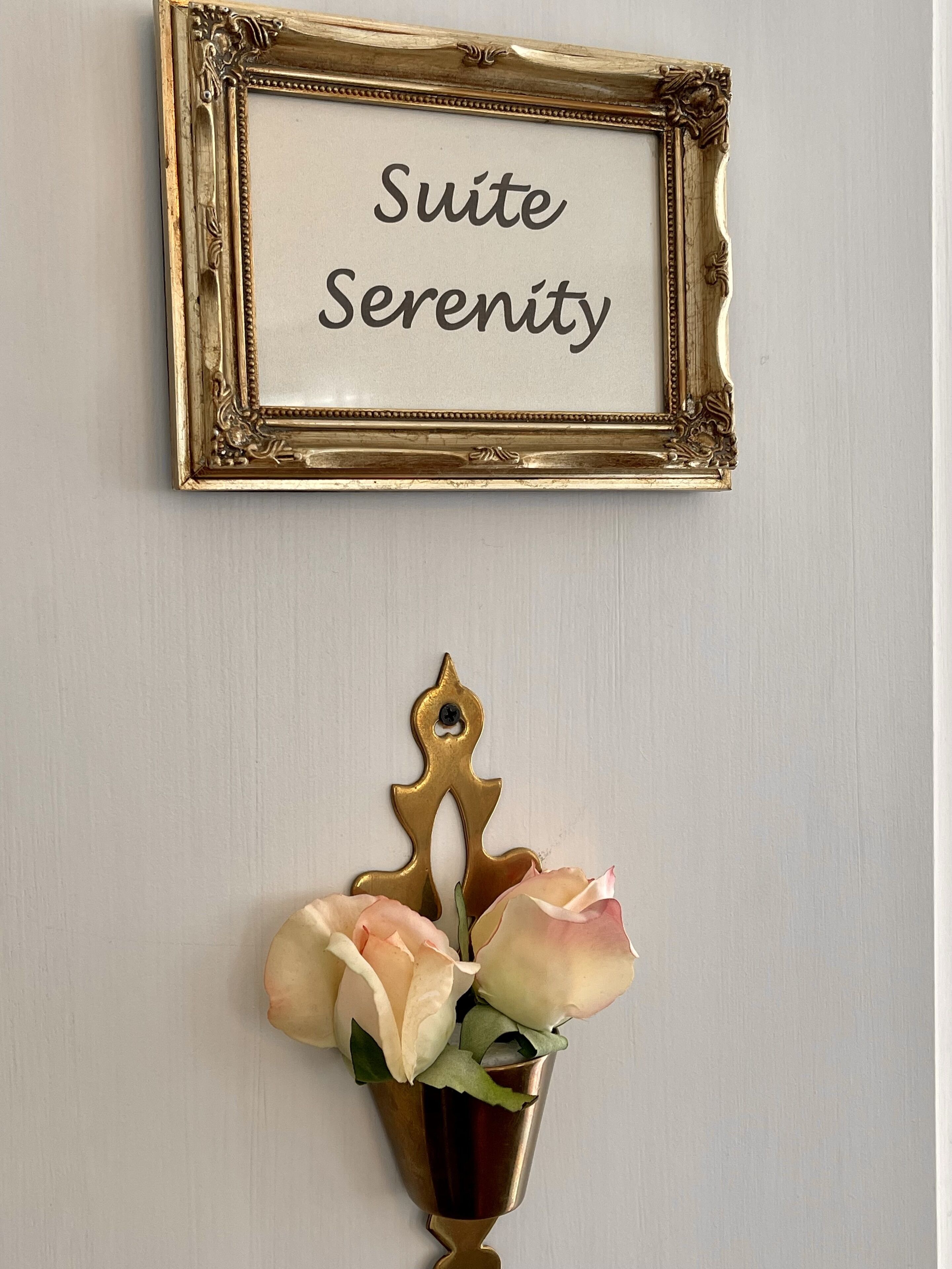 A gold-framed sign with the text "Suite Serenity" and a gold vase with roses.