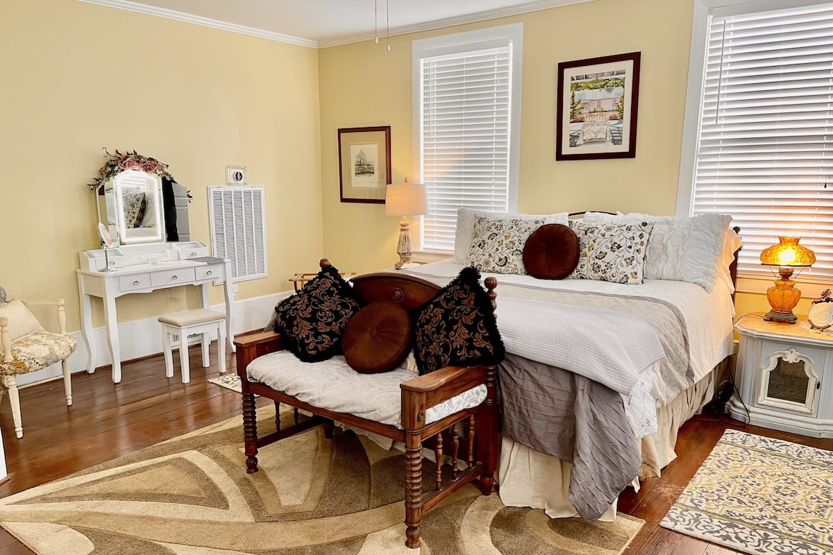 A bedroom with a bed, bedside table, lamp, dresser, mirror, and a chair.
