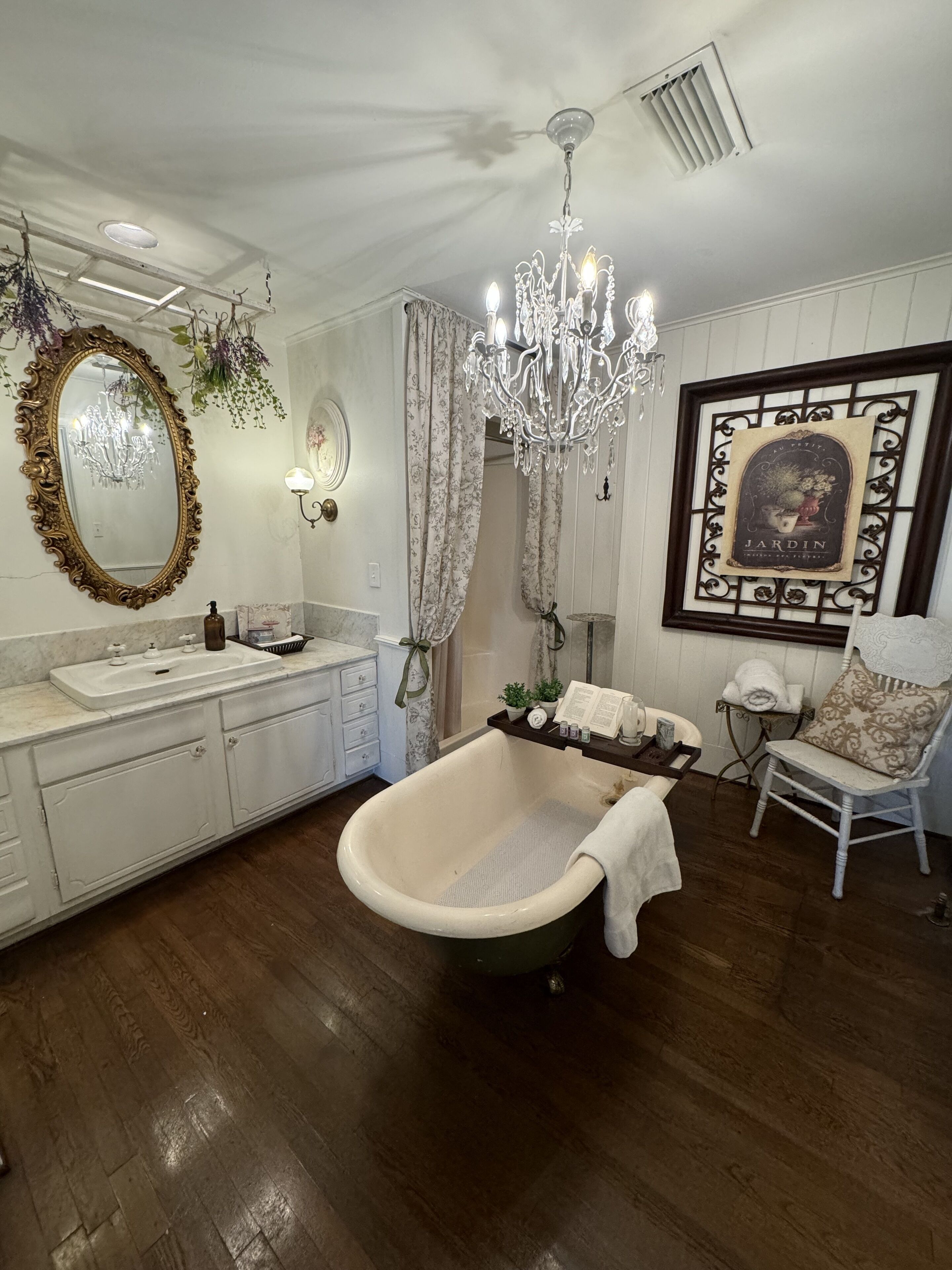 A bathroom with a freestanding bathtub, a vanity with a mirror, a chandelier, and a framed picture on the wall.