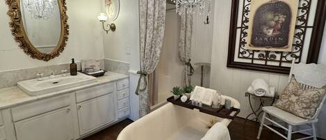 A bathroom with a freestanding bathtub, a vanity with a mirror, a chandelier, and a framed picture on the wall.