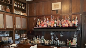 Eine Barbereich mit Holzvertäfelung, einer Auswahl an Spirituosenflaschen, Gläsern und einem Schild mit der Aufschrift 'The Whiskey There is No Cure For'.