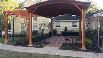 Ein überdachter Patio-Bereich mit einem Pflasterweg, einer Holz-Pergola und Gartenmöbeln.