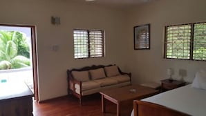 A room with a wooden sofa, a small table, and a bed. There are windows with metal bars and a view of greenery outside. - Ocho Rios Pimento Villas (Ocho Rios)